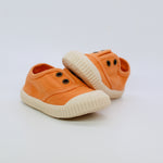 Pair of orange children's shoes with white soles on a light gray background
