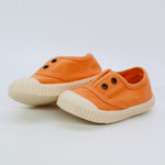 Pair of orange children's shoes with white soles on a light gray background