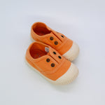 Pair of orange children's shoes with white soles on a light gray background