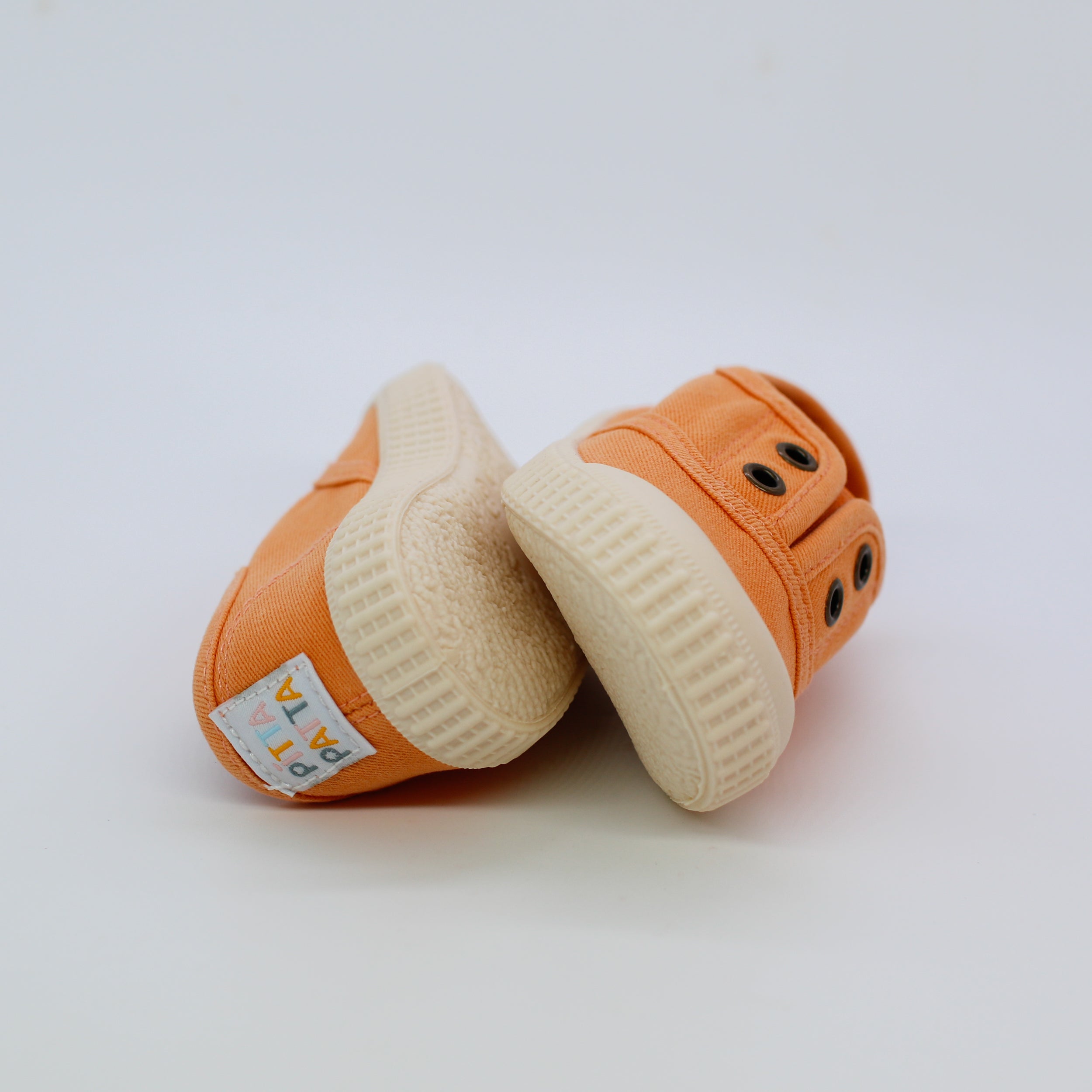 Pair of orange baby shoes with white soles on a light gray background