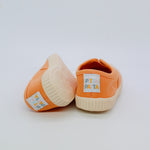 Pair of orange baby shoes with white soles on a light gray background