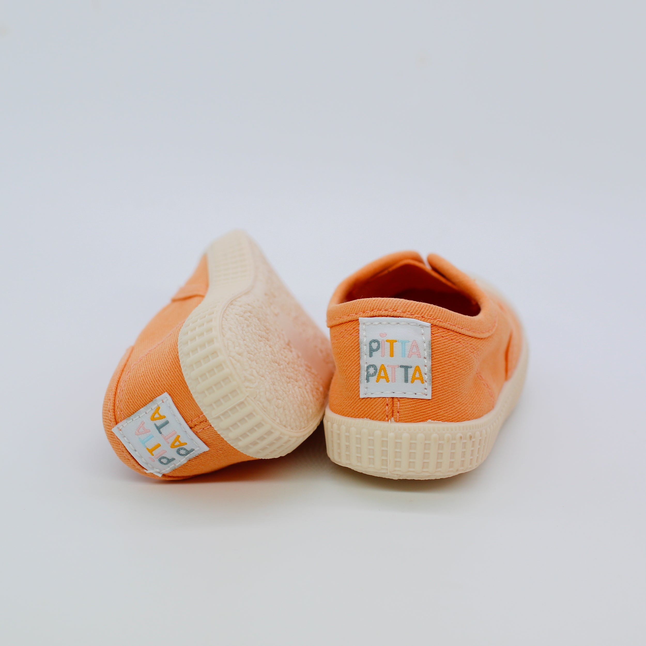 Pair of orange baby shoes with white soles on a light gray background