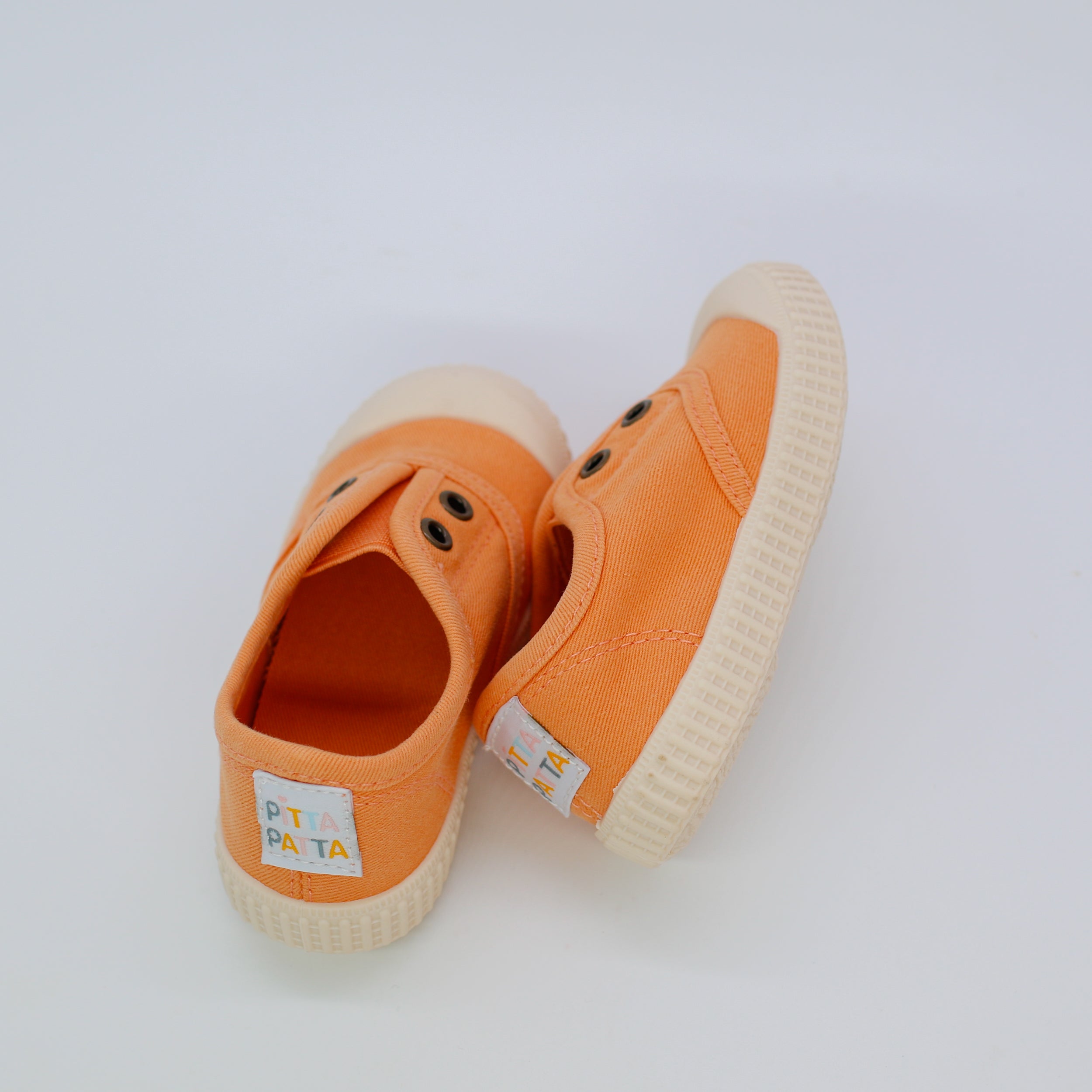 Orange children's shoes with white soles on a light gray background