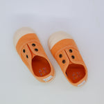 Pair of orange children's shoes with beige soles on a white background