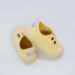 Pair of yellow children's shoes with brand labels on a light gray background