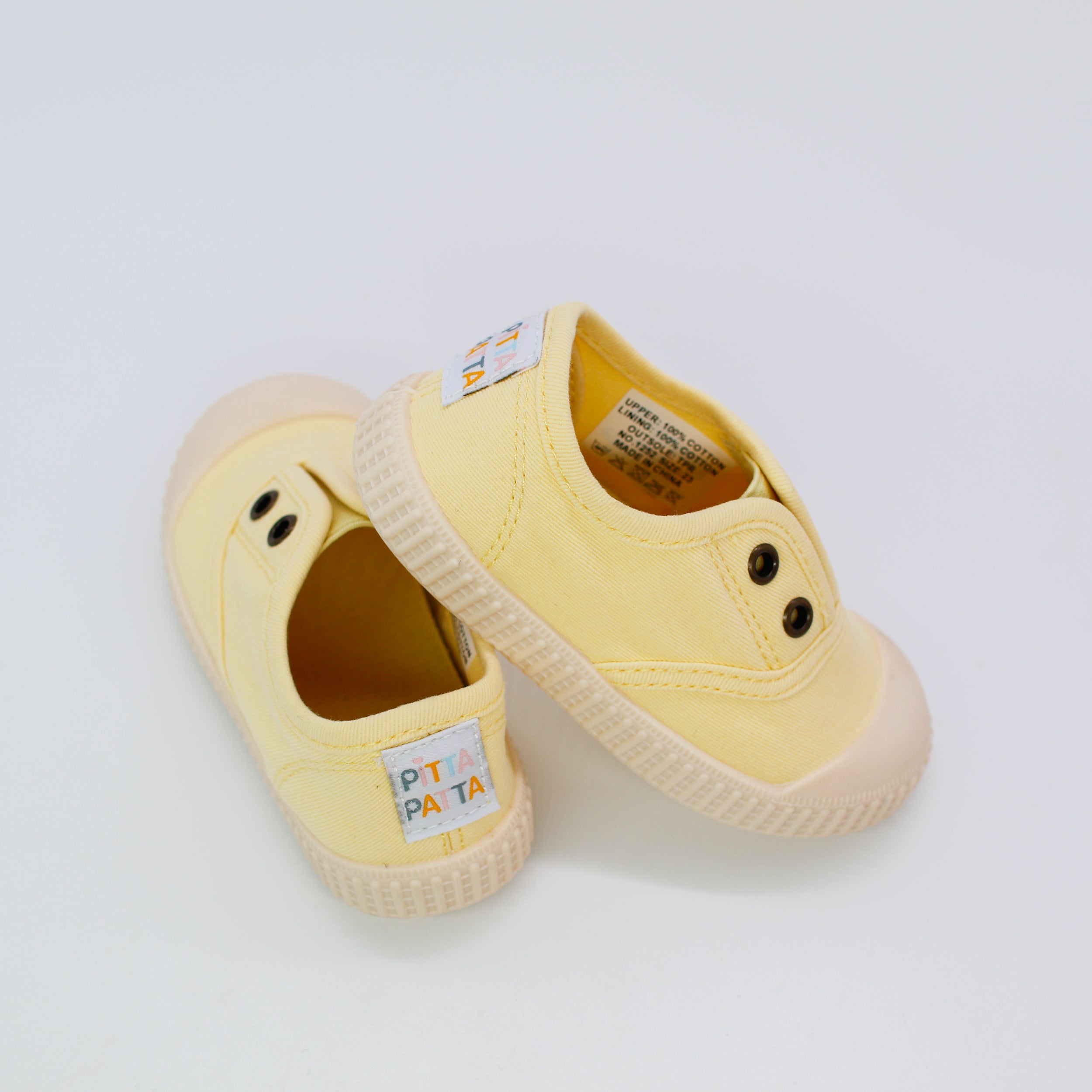 Pair of yellow children's shoes with brand labels on a light gray background