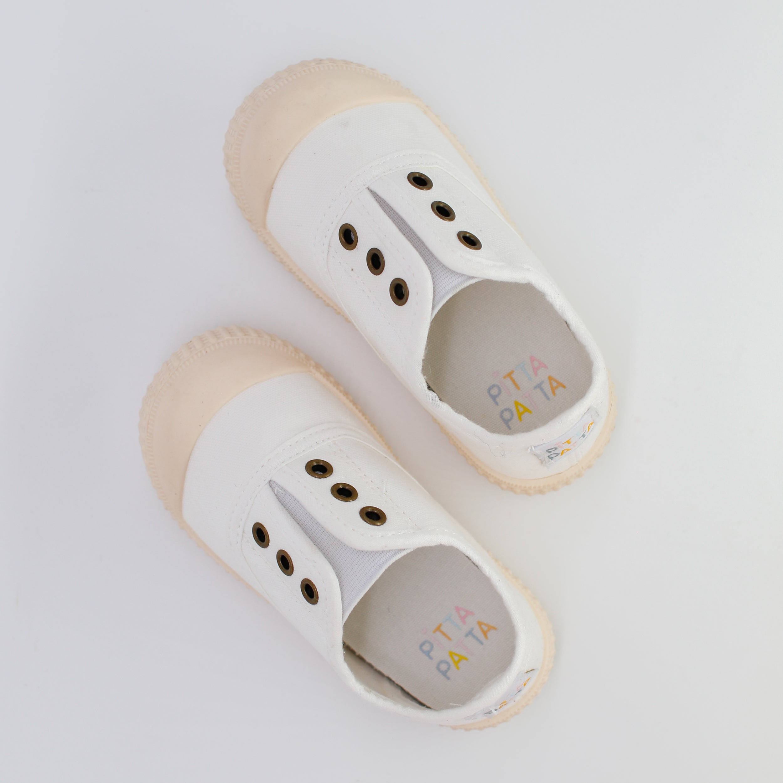 Pair of white children's shoes with beige soles on a light gray background