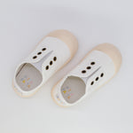 Pair of white children's shoes with beige soles on a light gray background