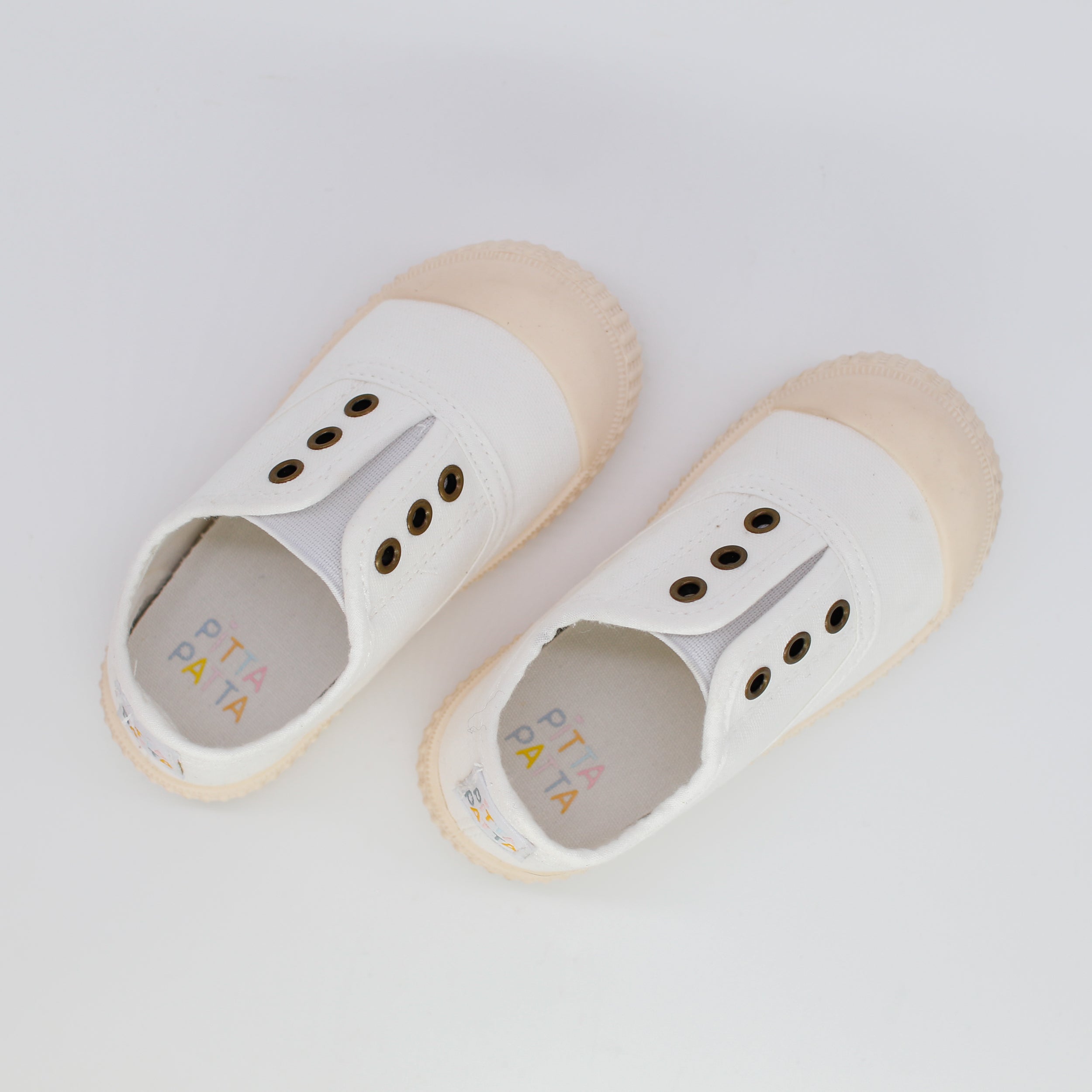Pair of white children's shoes with beige soles on a light gray background