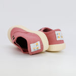 Pair of pink children's shoes with white soles on a light gray background