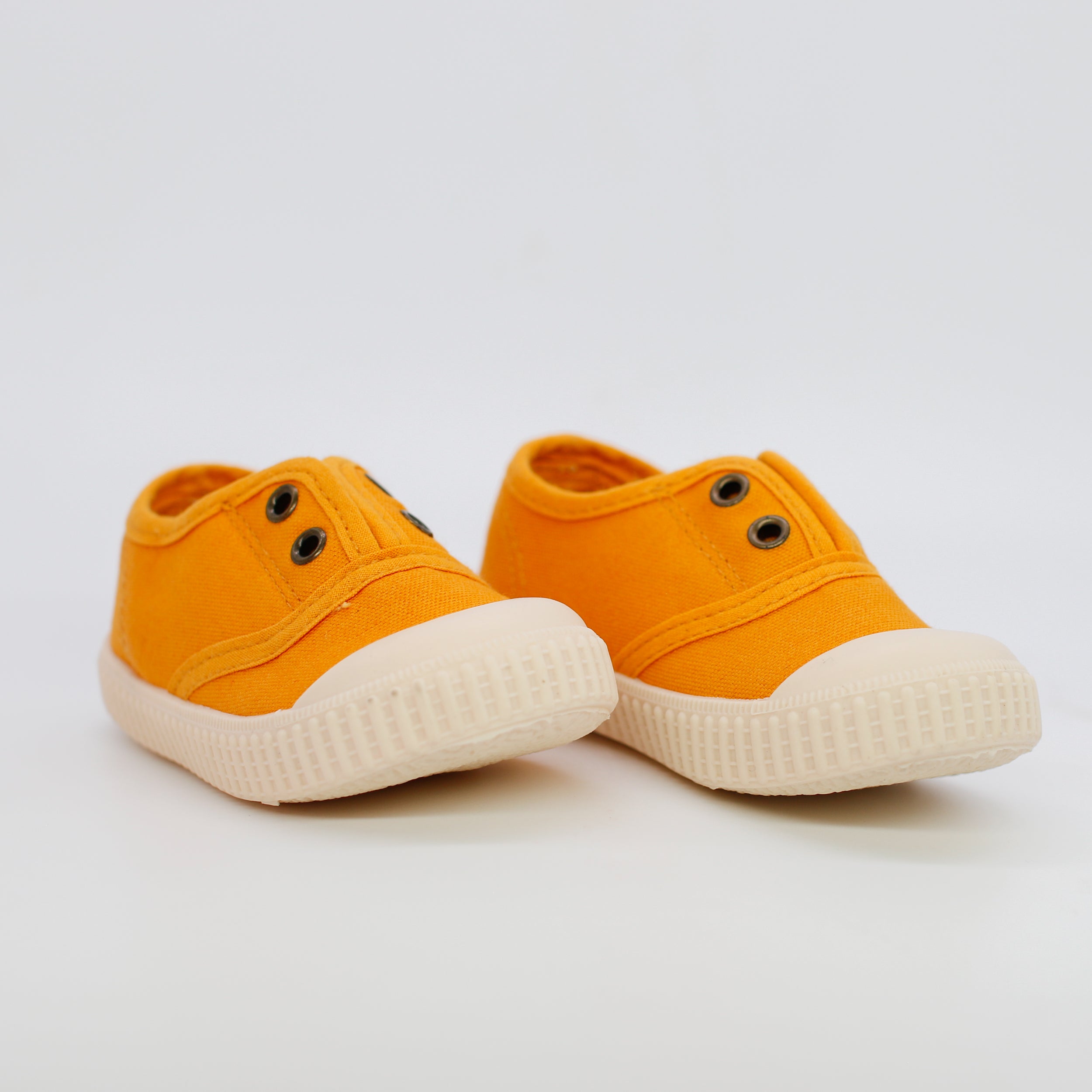 Pair of orange sneakers with white soles on a light gray background