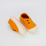 Pair of orange children's shoes with white soles on a light gray background