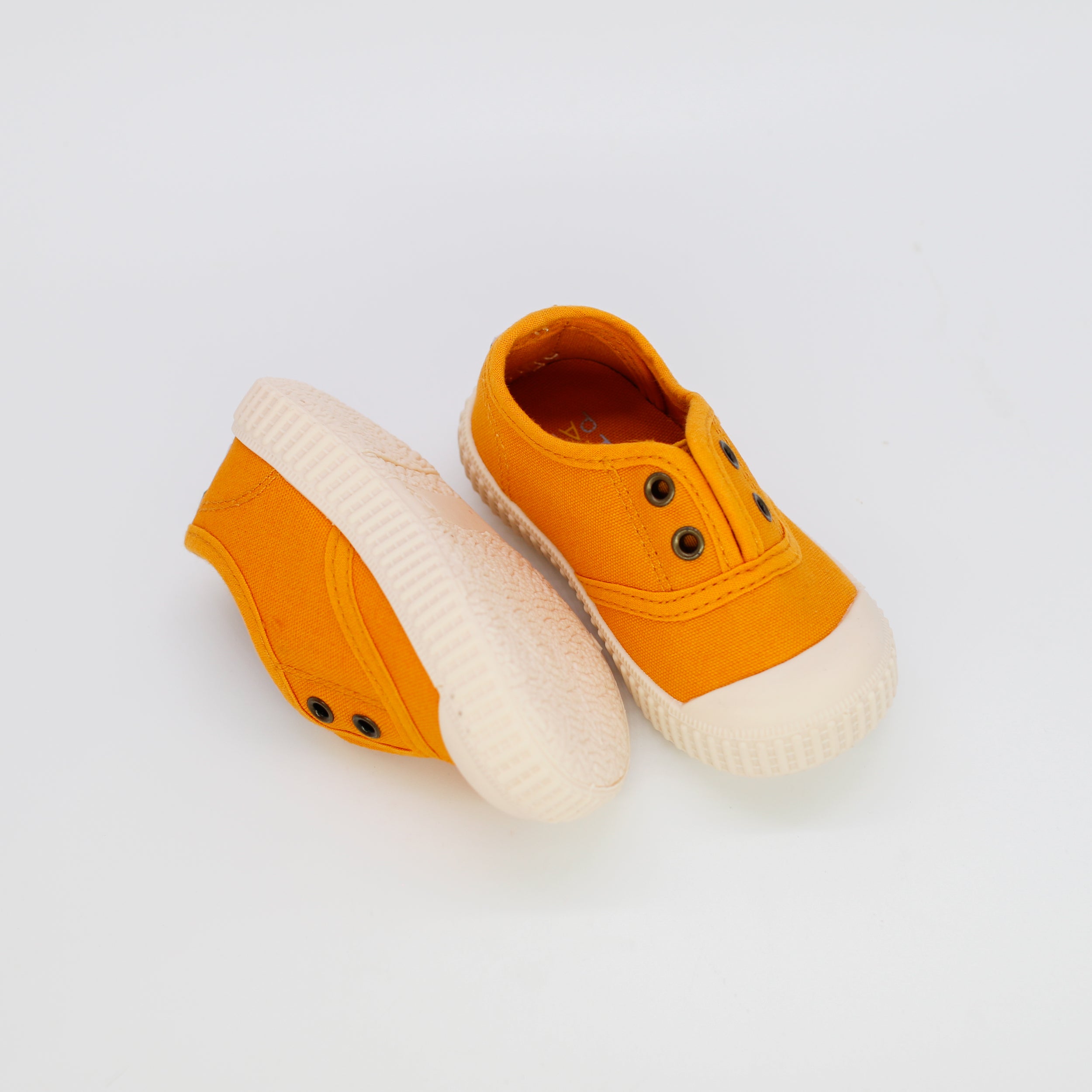 Pair of orange children's shoes with white soles on a light gray background