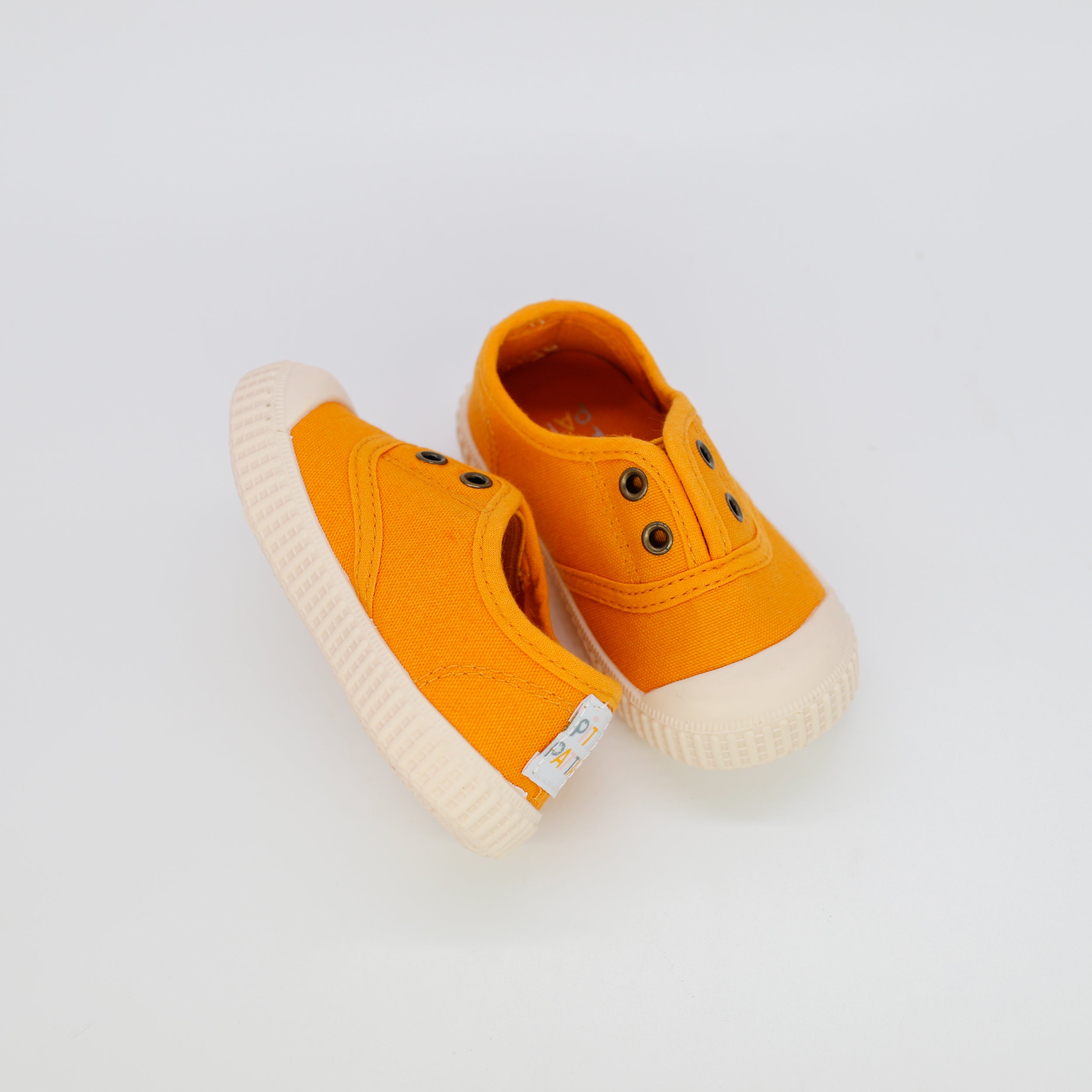 Pair of orange children's shoes with white soles on a light gray background