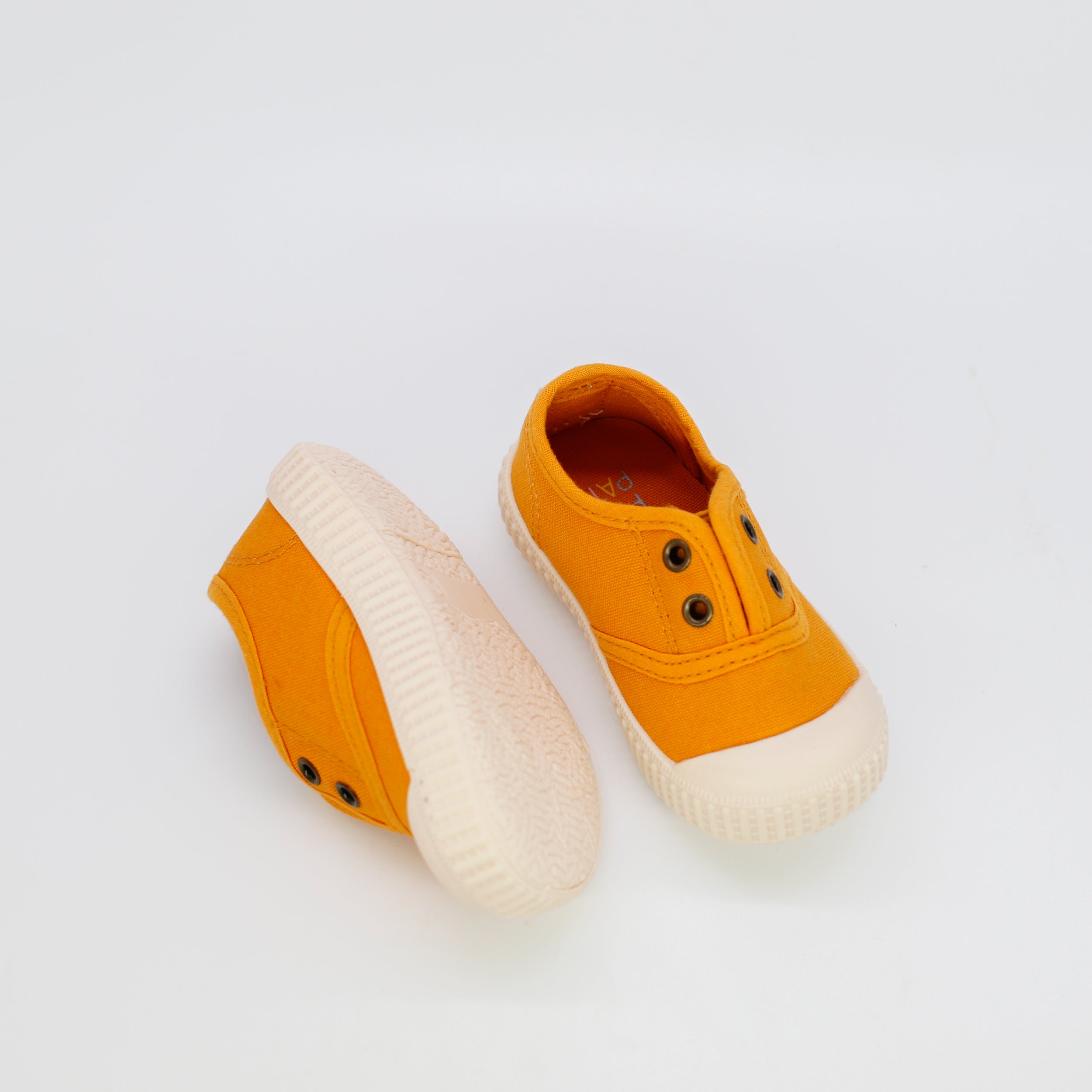 Pair of mustard yellow children's shoes with white soles on a light gray background